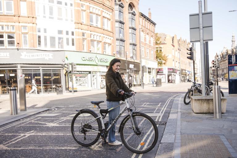 Young woman standing with bike on city street