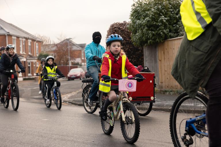 Group of adults and children in high vis riding cycles in road