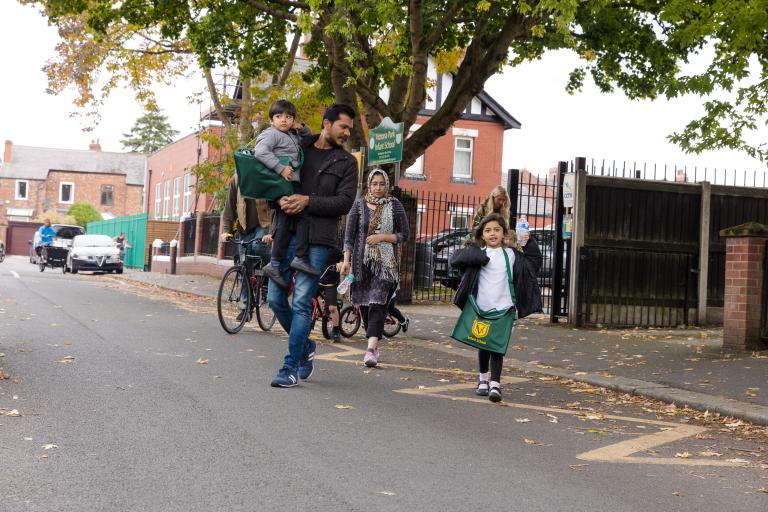 Children and parents walking and cycling on a street outside a school.