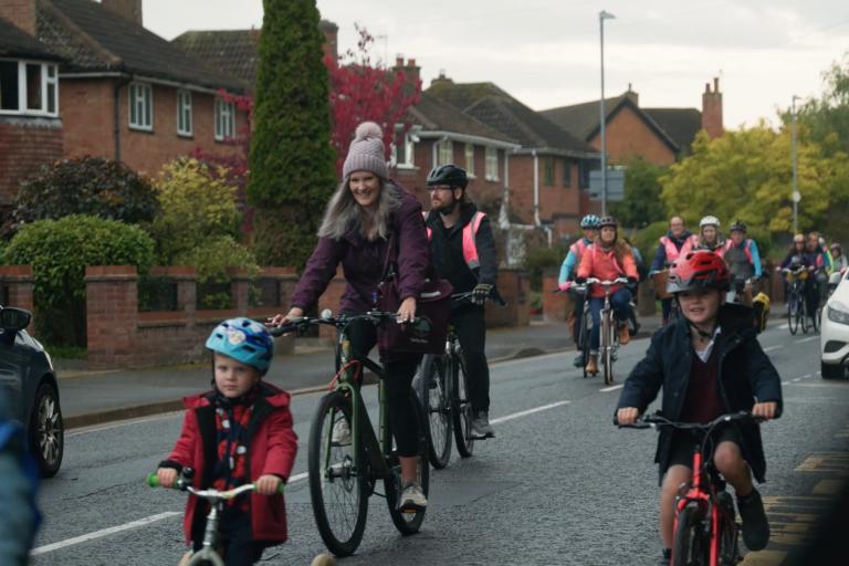 Children and adults cycle along a road on a residential street as a group.