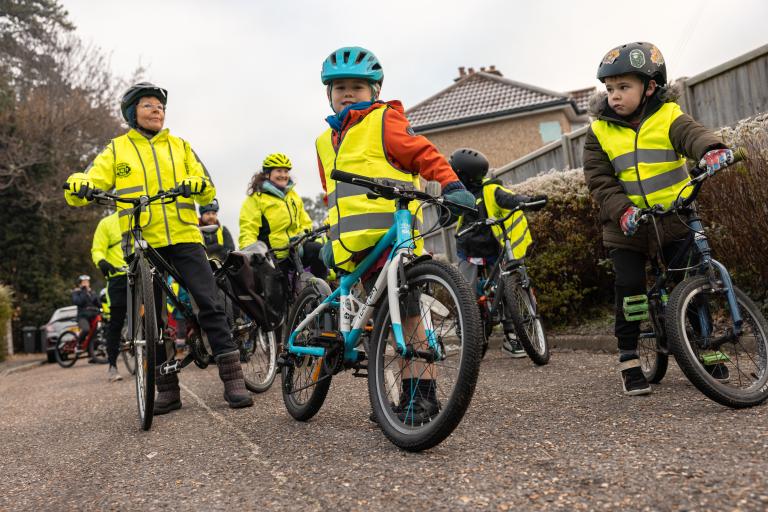 Young children wearing helmets in high vis riding cycles in road