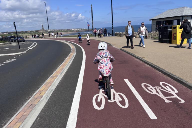 Child cycling on a cycle track separated from the road by a raised area. The track is two-way, with bicycles painted on the track to indicate this. This child is wearing a helmet.