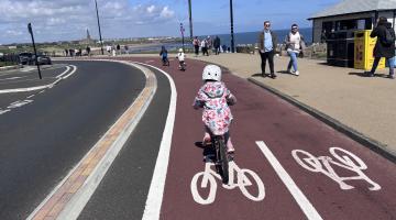 Child cycling on a cycle track separated from the road by a raised area. The track is two-way, with bicycles painted on the track to indicate this. This child is wearing a helmet.